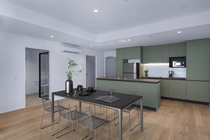 Inside a new home at Victoria Street, Flemington, kitchen area with kitchen table and bench with cupboards behind all on timber floors