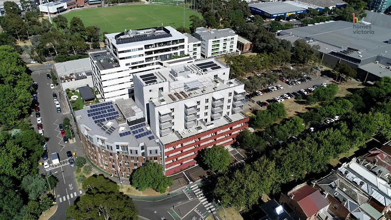 Top view image of building with solar Pannel on it and the building surrounded with trees, beautiful oval, road with car park and houses around