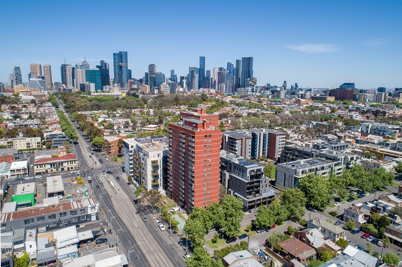 A drone image of red brick tall building surrounded by houses, trees and roads