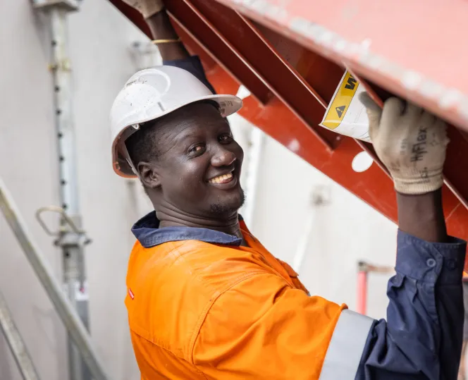 Builder wearing a hard hat and hi-vis jumper with a steel ladder in his hands smiling in the camera