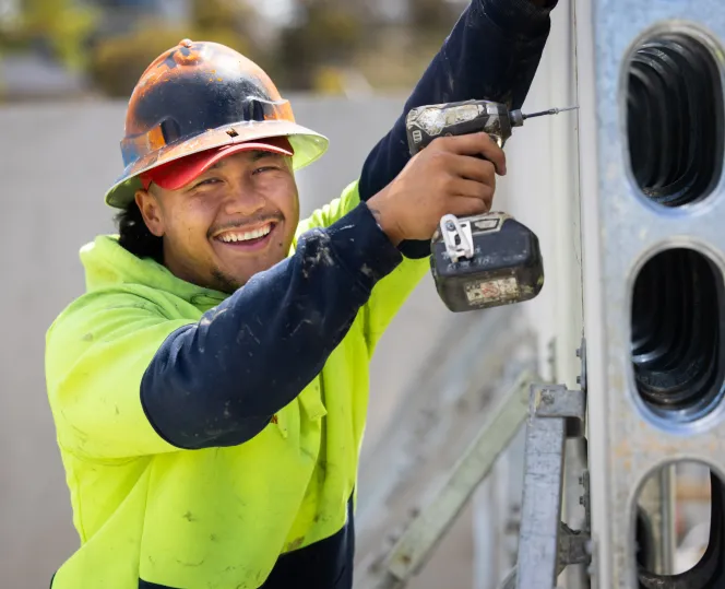 Builder wearing a hard hat and hi-vis jumper with a drill in his hand smiling in the camera