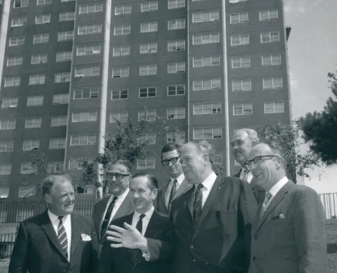 Black and white image of many people discussing in front for community housing