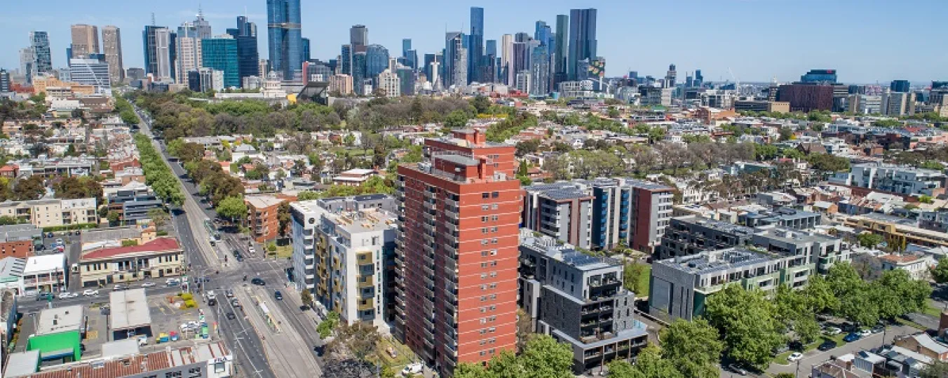 A drone image of red brick tall building surrounded by houses, trees and roads